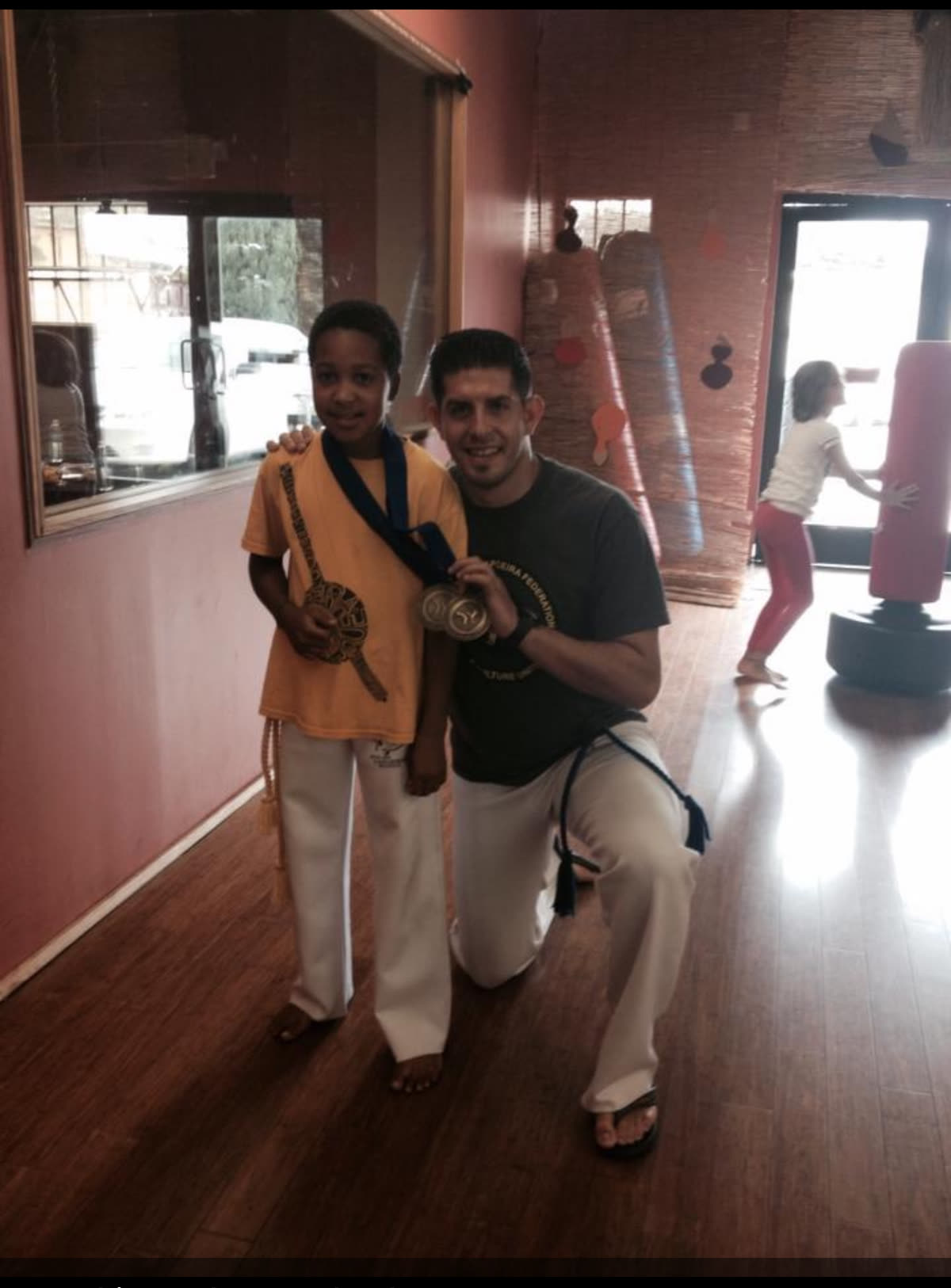 Young Miles Walker with his teacher in the studio after a class, both holding medals